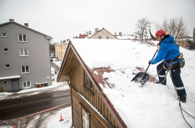 Lume eemaldamine katuselt elamul – töötaja puhastab kaldkatust turvatrossiga